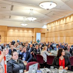 Photo from the 2023 Manufacturing USA Annual Meeting. Woman holding a microphone asking a question with attendees in the background.