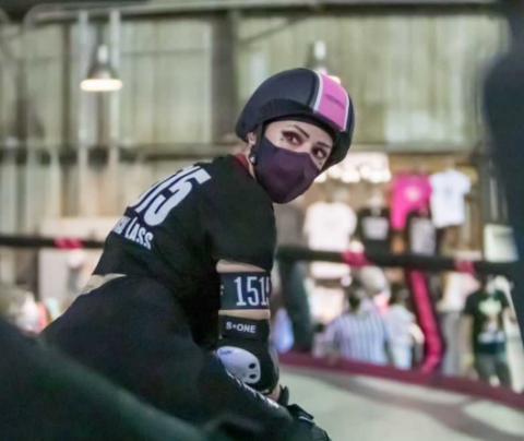 Photo of Diana Mercado Gruber doing roller derby wearing a helmet with a pink strike down the center