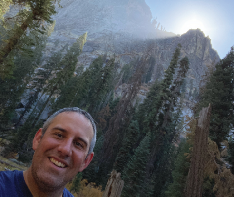 Photo of Samuel Moyer with mountains and pine trees behind him.