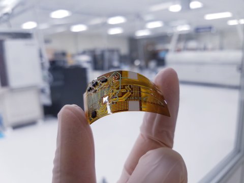 Photo of two gloved fingers holding up a NextFlex microcontroller. Photo credit: NIST