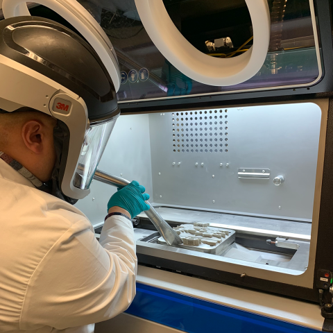 Photo of a technician wearing a 3M mask vacuuming dust inside of an additive manufacturing machine