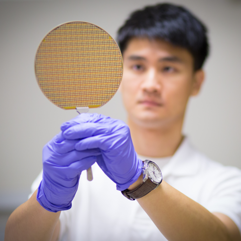 Photo of someone in wearing purple gloves holding up a silicon wafer