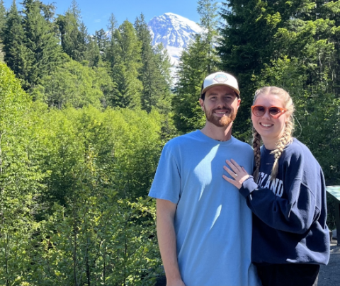 Photo of Emily Molstad and her fiance on a hike with a snow capped mountain in the background