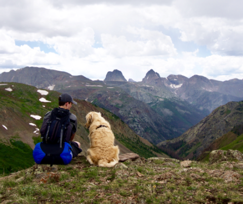 Photo of Isaac Sloan and his dog sitting sitting on top of a hill looking out at mountains